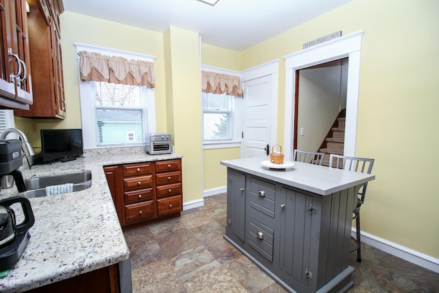 kitchen with a breakfast bar, sink, a kitchen island, and light stone counters