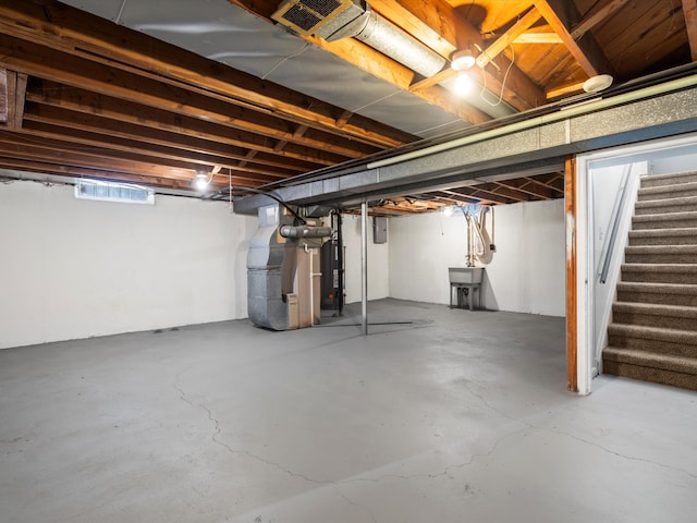 basement featuring water heater, sink, and heating unit