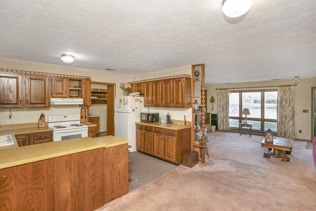 kitchen with a textured ceiling, kitchen peninsula, light colored carpet, and white appliances