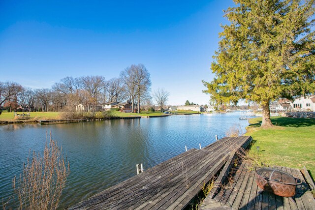 view of dock with a water view, an outdoor fire pit, and a lawn