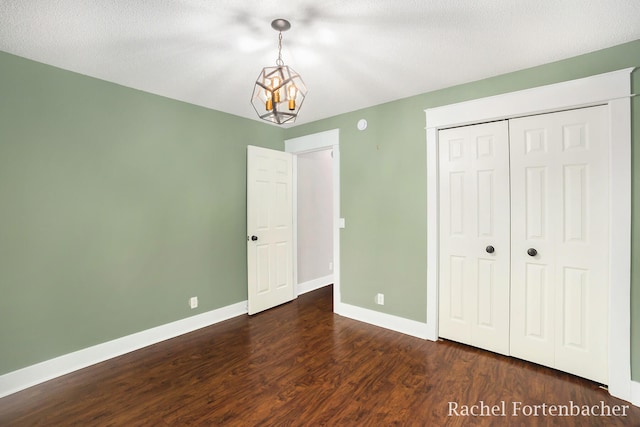 unfurnished bedroom featuring a textured ceiling, dark hardwood / wood-style floors, an inviting chandelier, and a closet