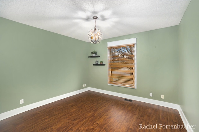 unfurnished room with hardwood / wood-style floors, a textured ceiling, and an inviting chandelier