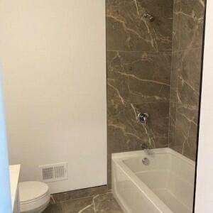 bathroom featuring tile patterned floors, tiled shower / bath combo, and toilet