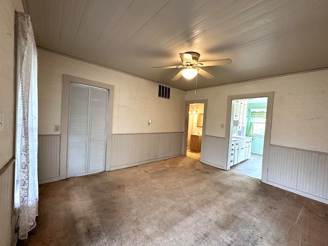 unfurnished bedroom featuring light carpet, ensuite bath, a closet, and ceiling fan