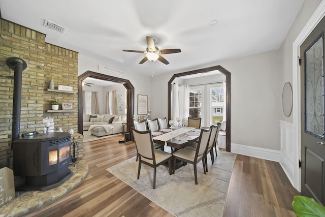 dining room featuring a wood stove, ceiling fan, and wood-type flooring