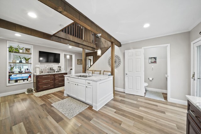 kitchen featuring white cabinetry, sink, an island with sink, light hardwood / wood-style floors, and decorative light fixtures