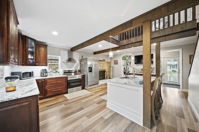 kitchen featuring sink, stainless steel appliances, wall chimney range hood, light stone counters, and light hardwood / wood-style floors