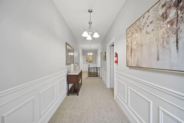 corridor featuring light colored carpet and an inviting chandelier