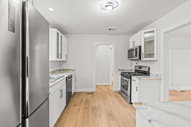 kitchen featuring white cabinets, sink, light stone countertops, light wood-type flooring, and stainless steel appliances