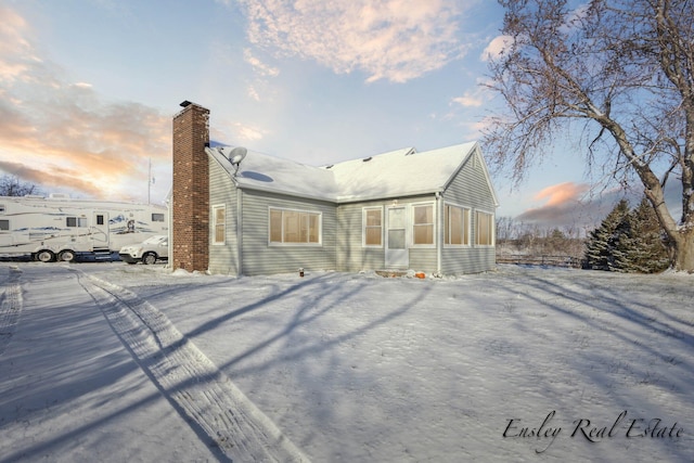 snow covered rear of property with a chimney and a sunroom