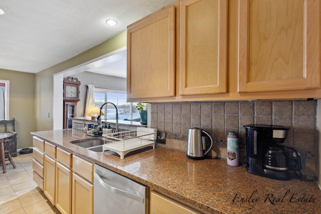 kitchen featuring stainless steel dishwasher, a sink, dark stone counters, backsplash, and light brown cabinets