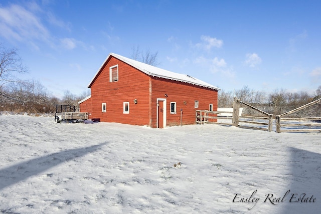 snow covered back of property with an outdoor structure, a barn, and fence