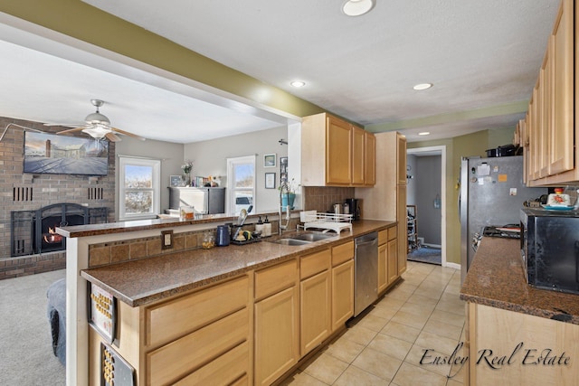 kitchen with light brown cabinetry, stainless steel appliances, a fireplace, a sink, and a peninsula