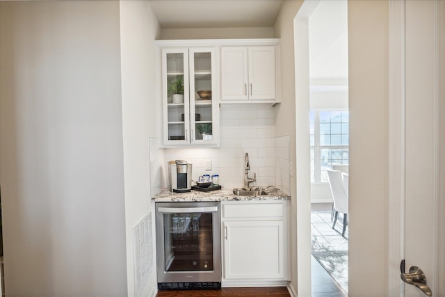 bar with wine cooler, white cabinetry, sink, and light stone counters