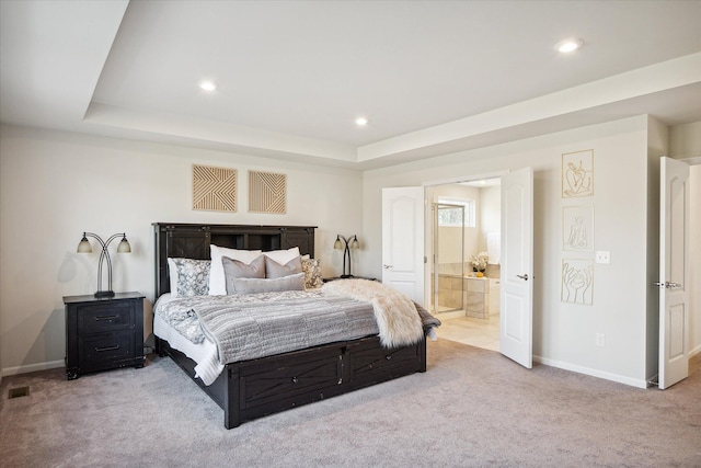 carpeted bedroom featuring a raised ceiling and ensuite bath