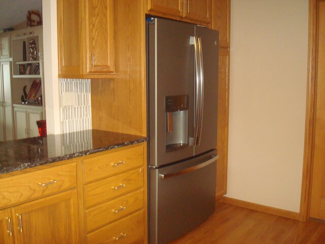 kitchen featuring stainless steel fridge, light wood-type flooring, and dark stone counters