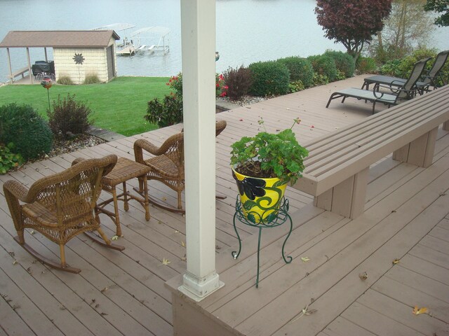 wooden deck with a water view, an outdoor structure, and a lawn