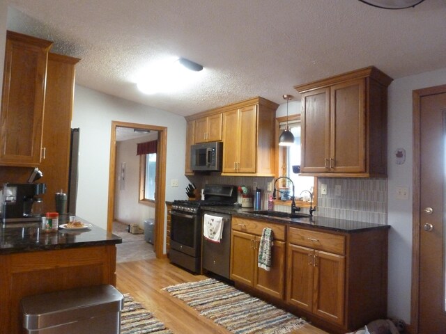 kitchen featuring hanging light fixtures, sink, decorative backsplash, light wood-type flooring, and appliances with stainless steel finishes