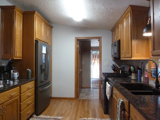 kitchen featuring a textured ceiling, vaulted ceiling, sink, black appliances, and light hardwood / wood-style floors