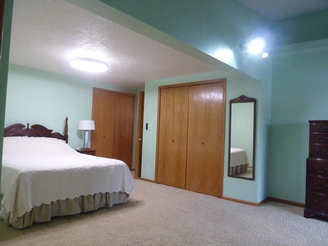 bedroom featuring a textured ceiling, light colored carpet, and two closets