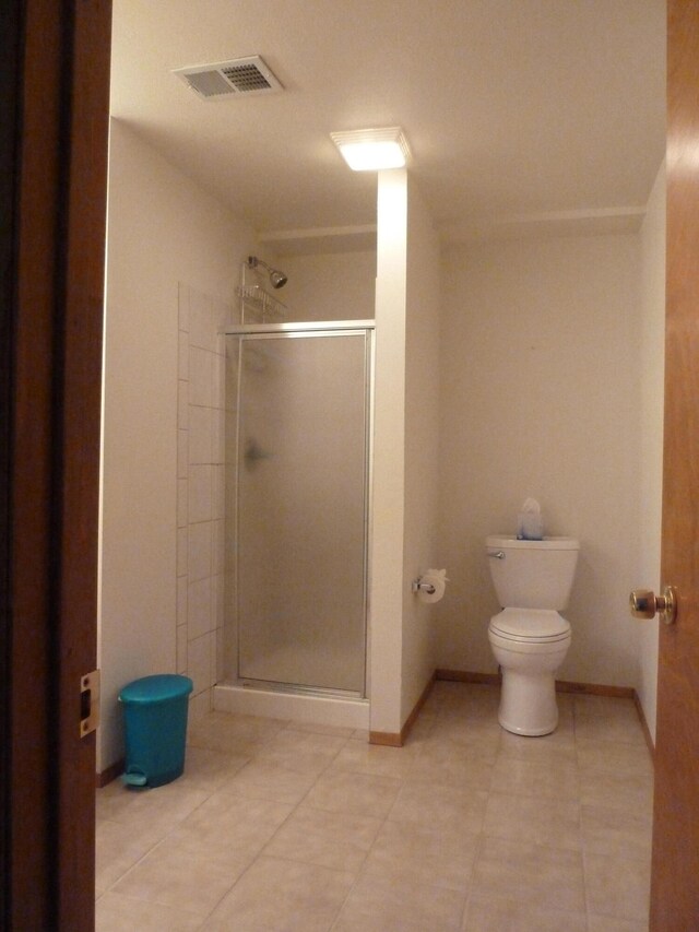 bathroom with tile patterned floors, toilet, and a shower with shower door