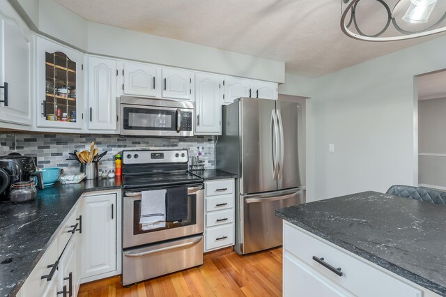 kitchen with white cabinets, backsplash, light wood-type flooring, and stainless steel appliances