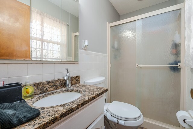 bathroom featuring a shower with door, vanity, tile walls, and toilet