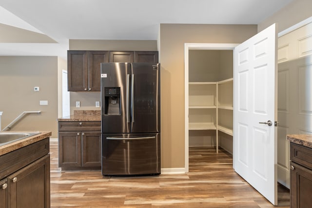 kitchen featuring stainless steel refrigerator with ice dispenser, light hardwood / wood-style flooring, dark brown cabinets, and sink