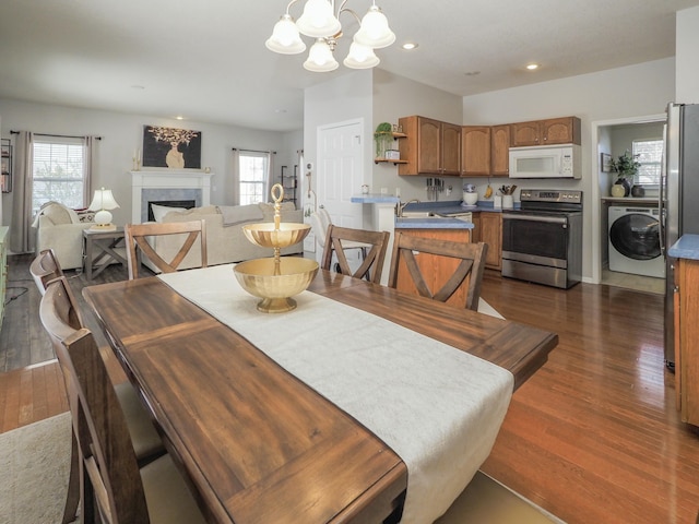 dining room featuring dark wood-type flooring, washer / clothes dryer, a healthy amount of sunlight, and a notable chandelier