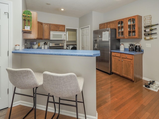 kitchen with kitchen peninsula, appliances with stainless steel finishes, a breakfast bar, dark wood-type flooring, and washer and dryer