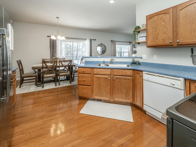 kitchen with an inviting chandelier, white dishwasher, sink, hanging light fixtures, and light hardwood / wood-style floors