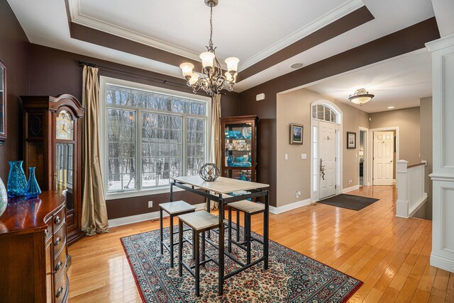 dining space featuring a notable chandelier, crown molding, a tray ceiling, and light hardwood / wood-style flooring