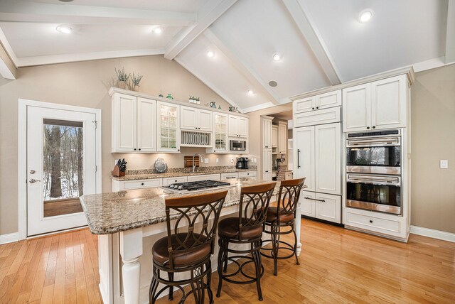 kitchen with light stone countertops, light wood-type flooring, white cabinets, a kitchen island, and a breakfast bar area