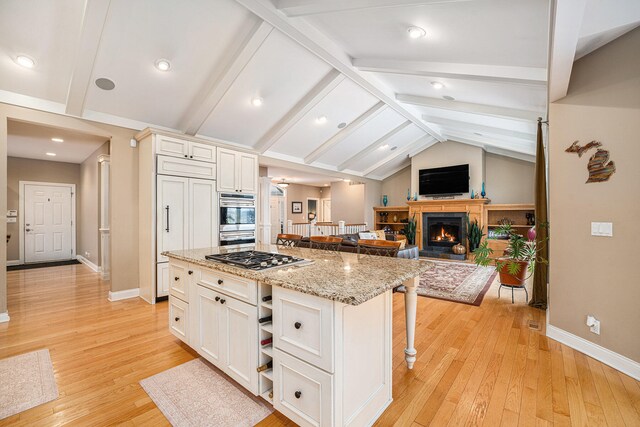 kitchen with light hardwood / wood-style flooring, vaulted ceiling with beams, a kitchen island, a kitchen bar, and stainless steel appliances