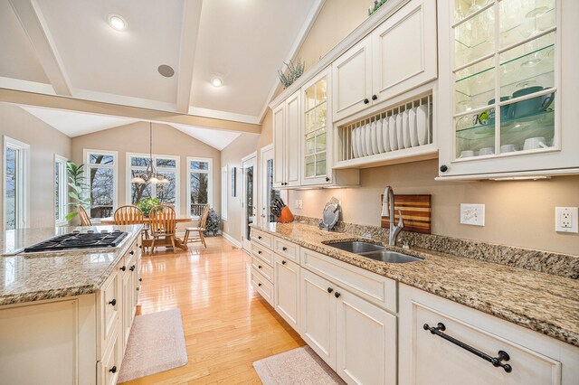 kitchen with vaulted ceiling with beams, light stone counters, light wood-type flooring, and sink