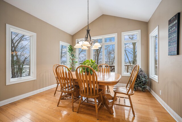 dining space with a chandelier, light wood-type flooring, a wealth of natural light, and lofted ceiling