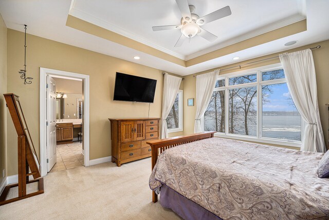 bedroom with ceiling fan, a raised ceiling, ensuite bathroom, light colored carpet, and ornamental molding