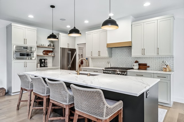 kitchen featuring a kitchen island with sink, sink, stainless steel appliances, and light hardwood / wood-style flooring