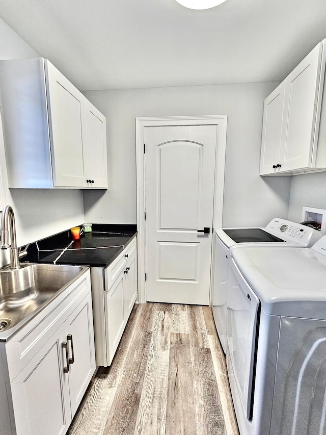 laundry area with sink, washer and clothes dryer, cabinets, and light wood-type flooring