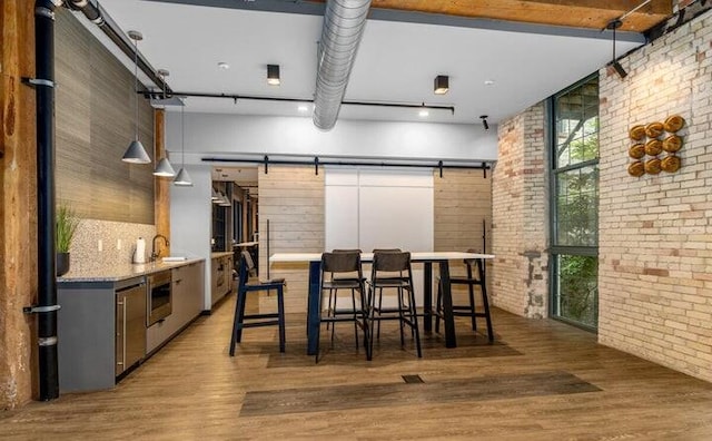 kitchen with hanging light fixtures, light stone counters, brick wall, a breakfast bar, and hardwood / wood-style flooring