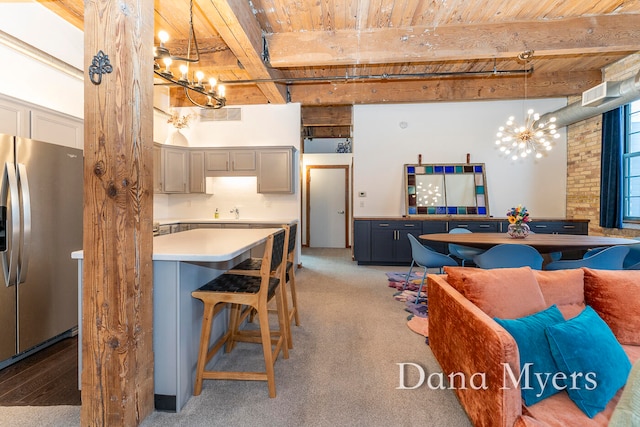 kitchen with gray cabinetry, light carpet, stainless steel refrigerator with ice dispenser, hanging light fixtures, and beam ceiling