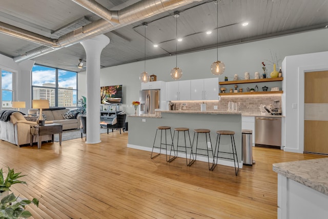 kitchen with pendant lighting, white cabinets, light hardwood / wood-style flooring, appliances with stainless steel finishes, and a breakfast bar area