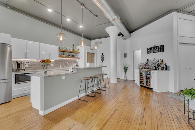 kitchen featuring stainless steel fridge, a towering ceiling, wine cooler, light hardwood / wood-style floors, and white cabinetry