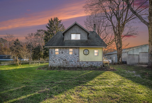 property exterior at dusk with a lawn and an outdoor structure