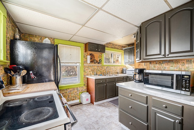 kitchen featuring dark brown cabinetry, sink, black fridge, stove, and a paneled ceiling