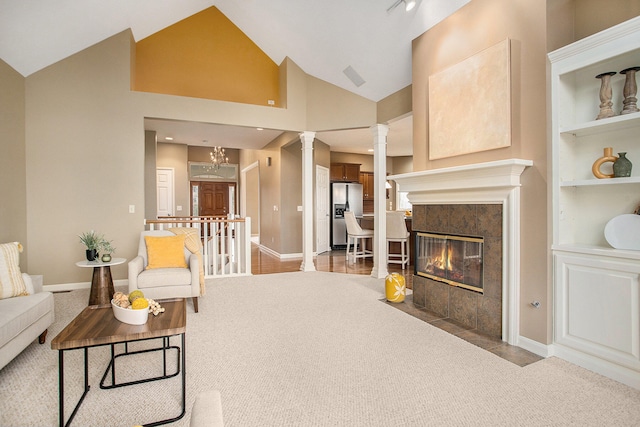 carpeted living room featuring high vaulted ceiling, a tile fireplace, an inviting chandelier, built in shelves, and decorative columns