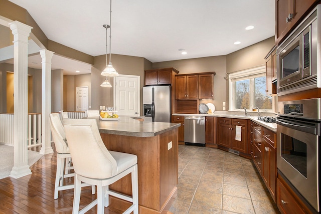 kitchen with a center island, hanging light fixtures, ornate columns, appliances with stainless steel finishes, and a breakfast bar area