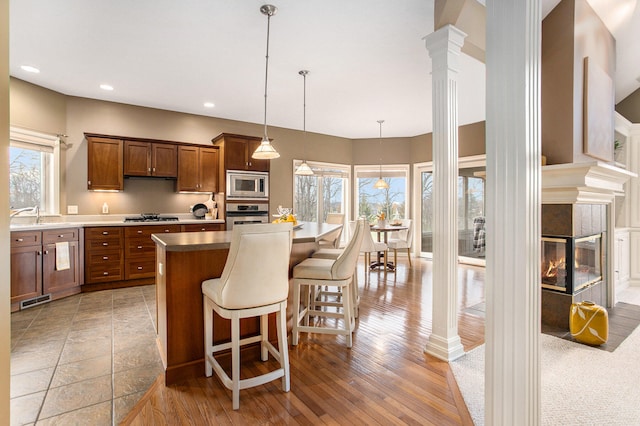 kitchen with appliances with stainless steel finishes, a breakfast bar, decorative light fixtures, hardwood / wood-style floors, and a tiled fireplace