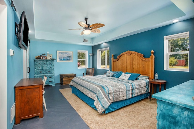 bedroom featuring ceiling fan, a raised ceiling, and multiple windows