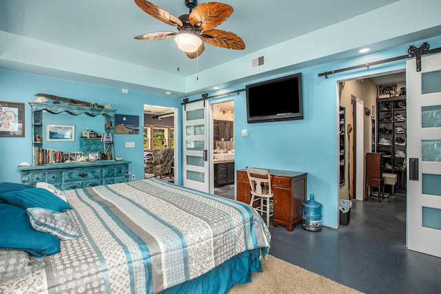 bedroom featuring a barn door, ensuite bath, and ceiling fan